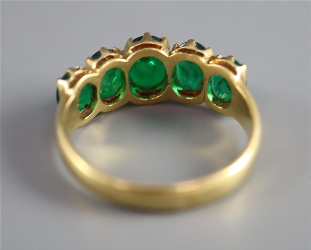 A mid to late 20th century gold and graduated five stone oval cut emerald set half hoop ring,
